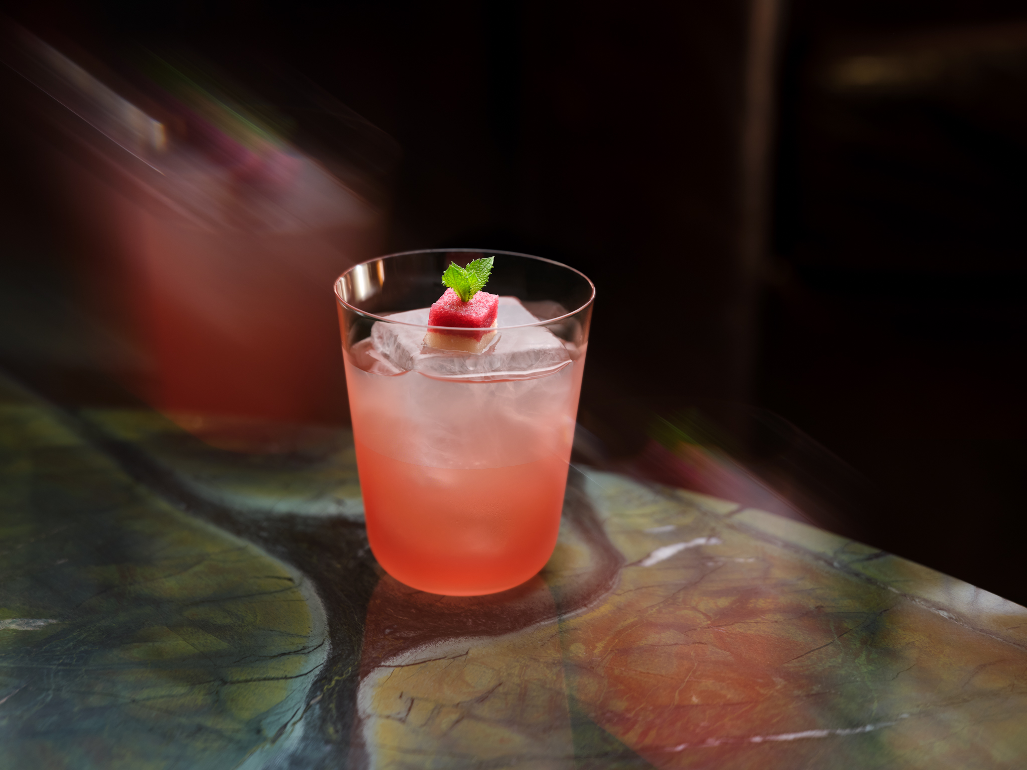A pink cocktail in a rocks glass garnished with mint