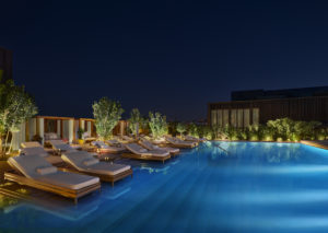 Rooftop pool with loungers lit at night