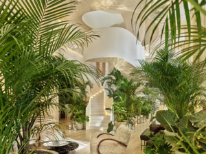 Bright lobby draped in potted tropical flora with white staircase