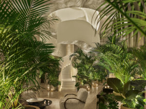 Bright lobby draped in potted tropical flora with white staircase