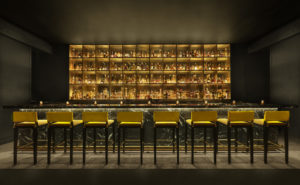 Bar with large backlit display case and row of stools