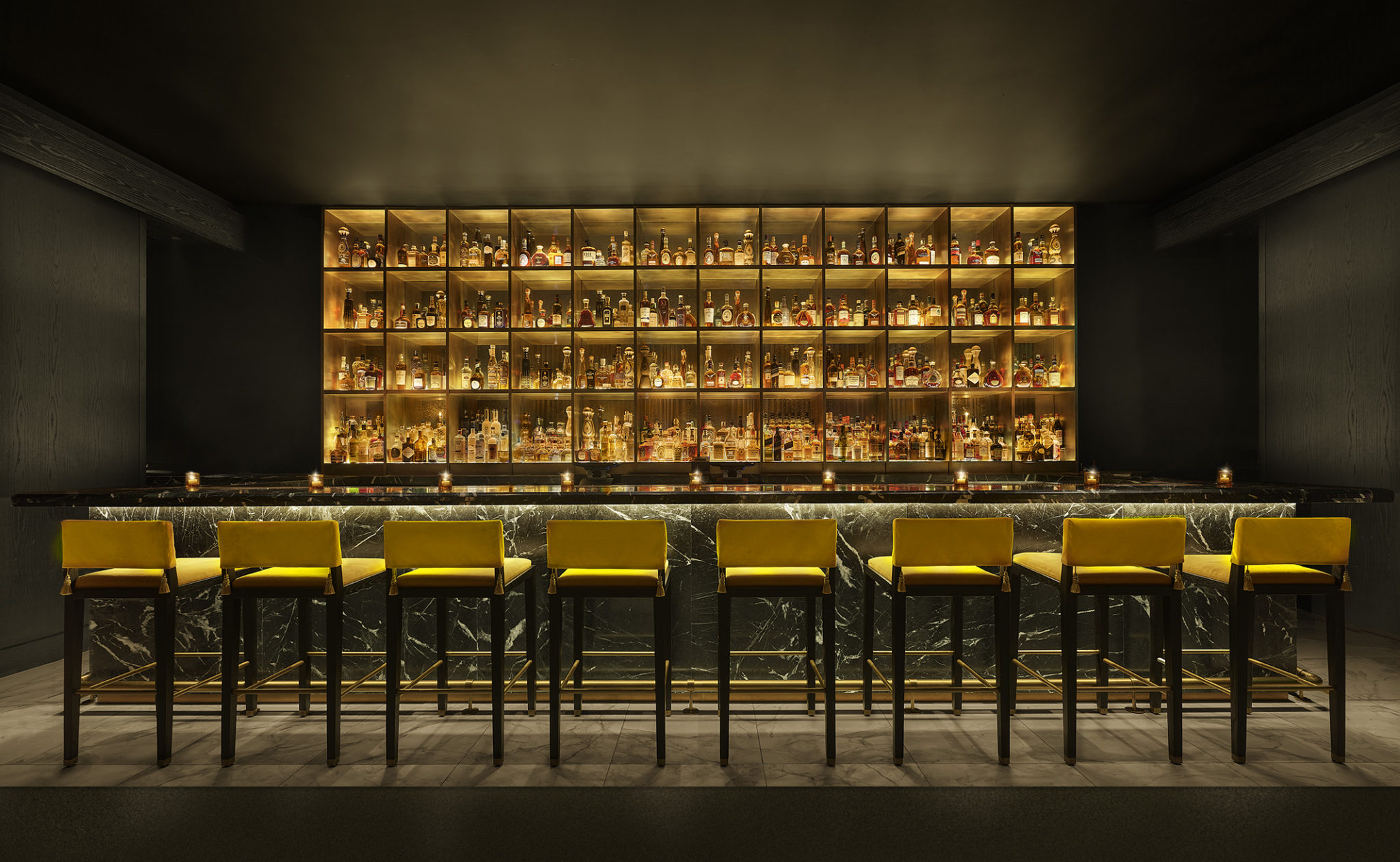 Bar with large backlit display case and row of stools