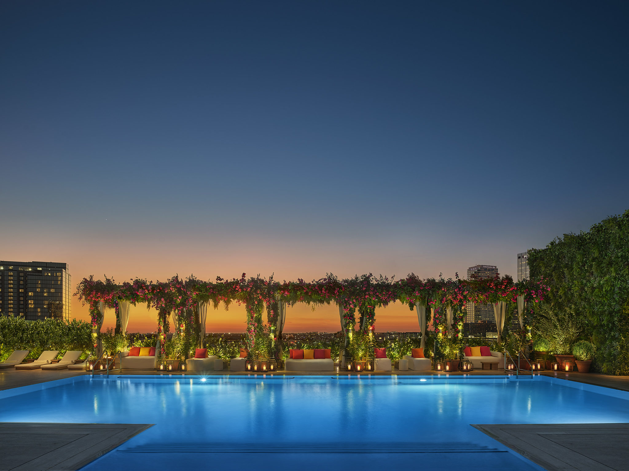 Lit pool lined with floral vine covered gazebo lounge space at night
