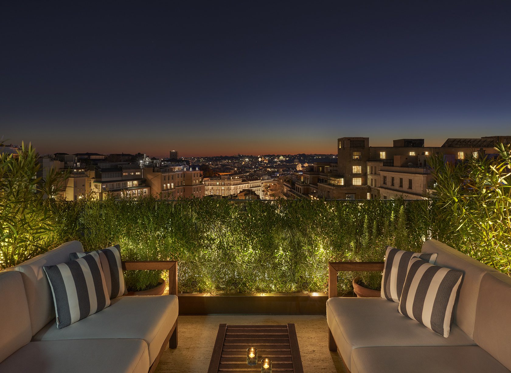 A nighttime view of two outdoor couches on a roof with city views in the distance.
